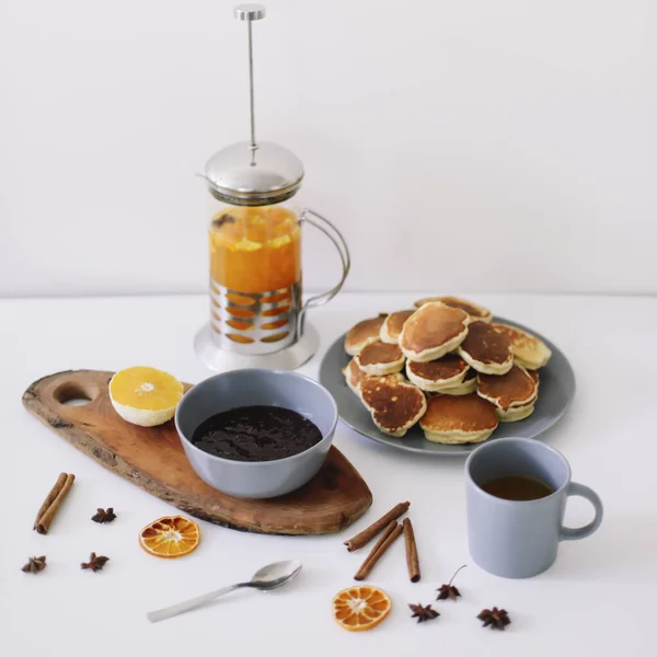 Pancake mewah dan teko teh dengan rempah-rempah, secangkir teh dengan jeruk, kayu manis, adas. Sarapan lezat dengan latar belakang putih. Selamat pagi. — Stok Foto