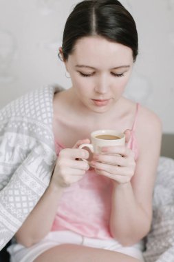 Sabahları genç bir bayanın elinde bir fincan kahve. Yatakta kahve içen güzel bir genç kızın portresi..