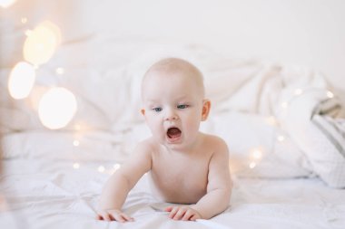 Karnını doyuran küçük bir çocuk. Sevimli bebek beyaz yatak odasında emeklemeyi öğreniyor. Yatakta yatan sevimli komik bebek.. 