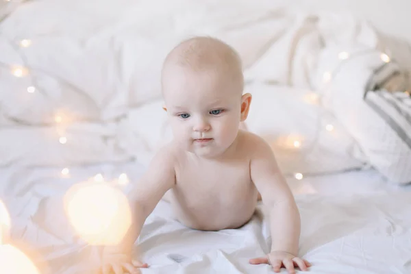 Pequeño niño haciendo tiempo de barriga. Adorable bebé aprendiendo a gatear en el dormitorio blanco. Lindo bebé divertido acostado en la cama . — Foto de Stock