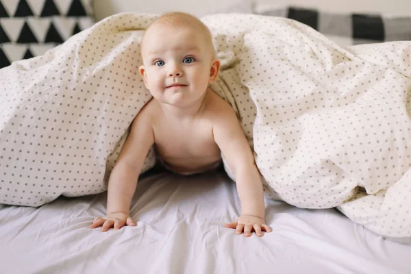 Dziecko odsiaduje wyrok w brzuszku. Urocze dziecko uczy się czołgać w białej sypialni. Cute śmieszne dziecko leżące na łóżku. — Zdjęcie stockowe