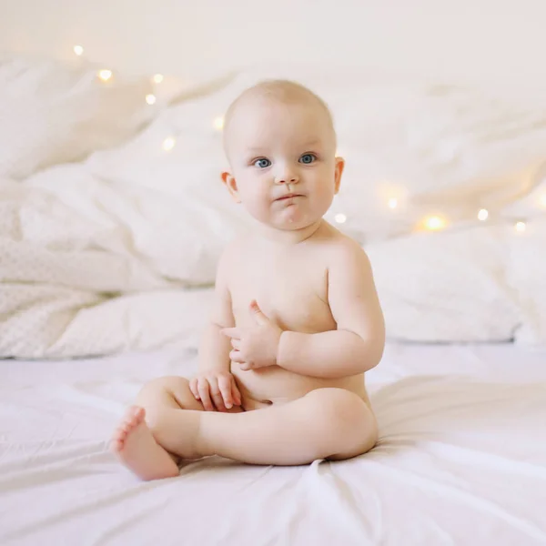 Carino bambino sorridente siede sul letto. felice bambino nudo. bambini di età inferiore a un anno. bambina che gioca, sorride, posa sul letto — Foto Stock