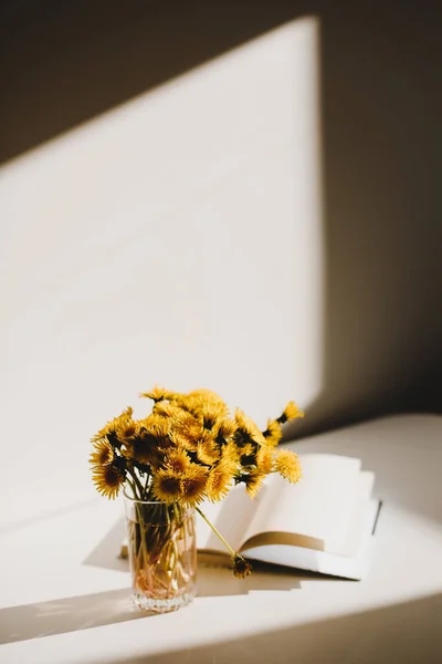 A book and a bunch of yellow dandelions.  Still life with wild flowers.  Play of light and shadow. Summer flowers