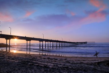 San Diego, Kaliforniya'da pier yakınındaki Ocean Beach üzerinde bir sörfçü yürür.