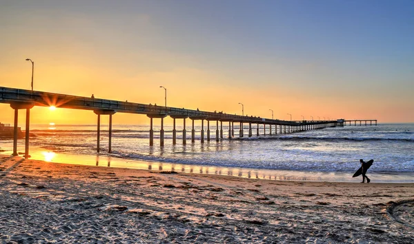 San Diego, Kaliforniya'da pier yakınındaki Ocean Beach üzerinde bir sörfçü yürür.