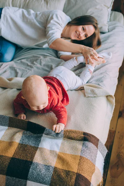 Uma jovem mãe senta-se em uma cama e veste meias brancas para um bebê — Fotografia de Stock