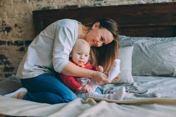 Uma jovem mãe senta-se em uma cama e veste meias brancas para um bebê — Fotografia de Stock