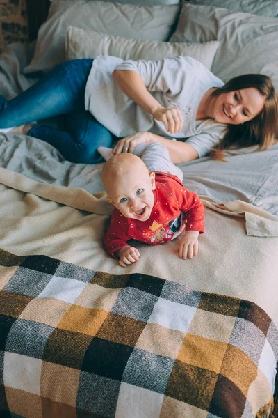 Maternidade. Uma jovem mãe com sua filha deitada na cama a brincar — Fotografia de Stock