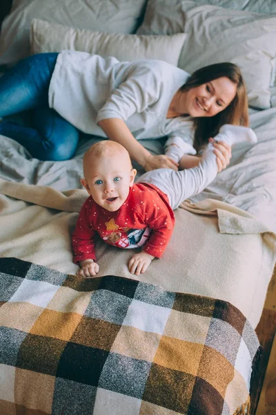 Moderskap. En ung mor med sin lilla dotter spelar ligger på sängen — Stockfoto