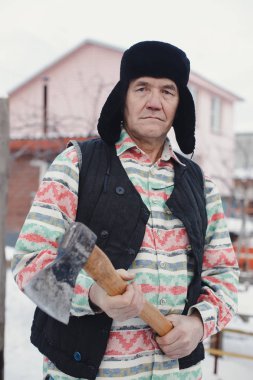 yaşlı adam kış bahçesinde balta ile.