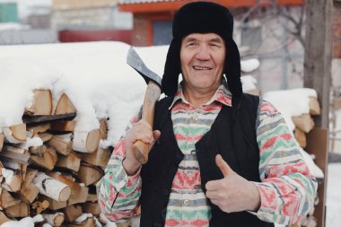 Elinde bir balta ile yaşlı adam gülümsüyor