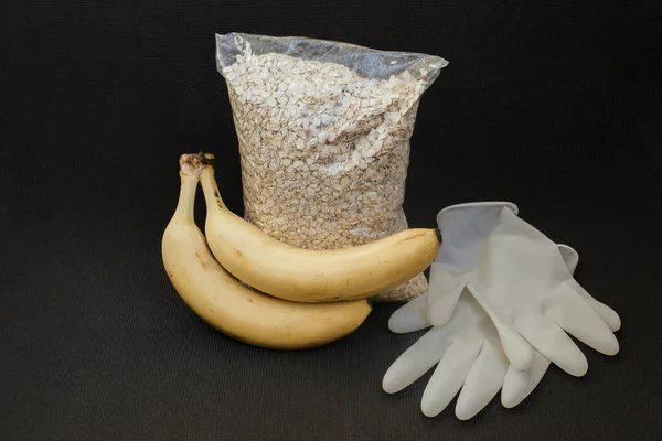 Food donation for people with the coronavirus pandemic. Food donations by volunteer in medical gloves to help isolate against coronavirus. Packet of oatmeal and gloves on a black insulated background
