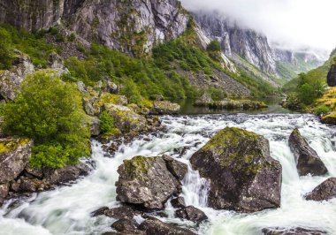 Yağmurlu bir günde akan bir dağ nehrinde kayalar.