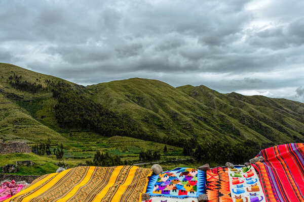 Colorful Peruvian carpets decorating a green Andes mountains vista under grey clouds