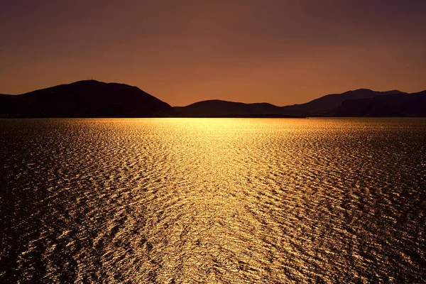 Темний бронзовий захід сонця з сонячними проблисками сонця на озері під чистим бронзовим небом — стокове фото