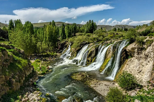 Kabarık beyaz ile mavi gökyüzü altında yeşil bir ortamda şelaleler
