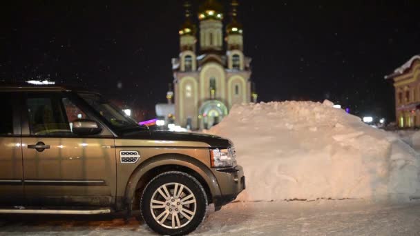 A háttérben a templom közelében parkoló gépkocsiban a havazás — Stock videók