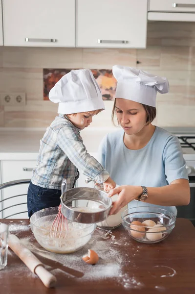 mother and child preparing dough on messy table at kitchen
