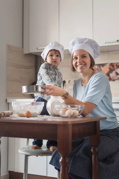 若い母親とキッチンで生地を準備する愛らしい小さな子  — 無料ストックフォト