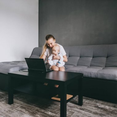 genç annenin bebeği ile kanepede otururken dizüstü bilgisayar kullanarak