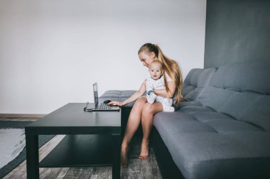 dizüstü bilgisayar kullanarak ve küçük çocuk kameraya bakarak tutan genç anne