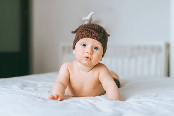 surprised emotional infant child in knitted deer hat in bed