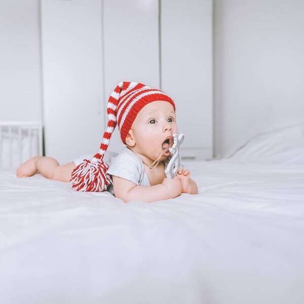 красивый младенец в полосатой красно-белой шляпе с игрушечным оленем в постели
