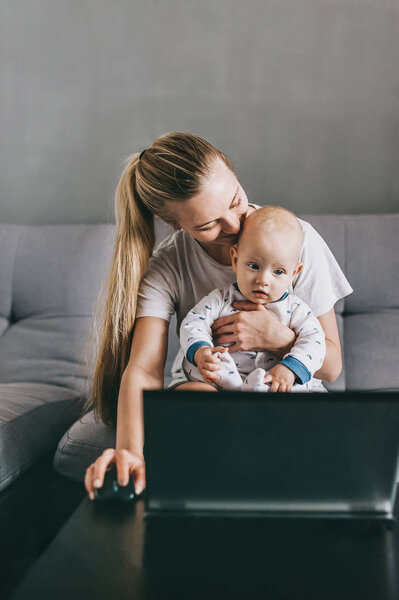 young mother and infant child using laptop together while sitting on couch at home