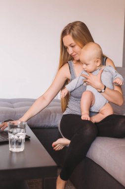 küçük bebek çocuk tutarak ve dizüstü bilgisayar kullanarak gülümseyen genç anne 