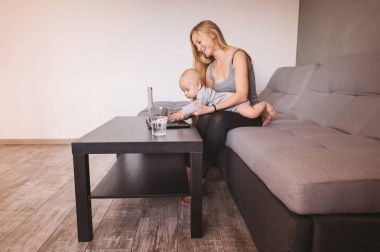 genç anne holding bebek çocuk oturma odasında dizüstü kullanarak gülümseyen yan görünümü