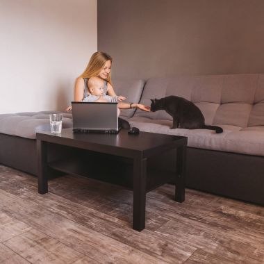 Anne ve süre kanepede oturan ve dizüstü bilgisayar kullanarak siyah kedi seyir şirin bebek çocuk gülümseyen 