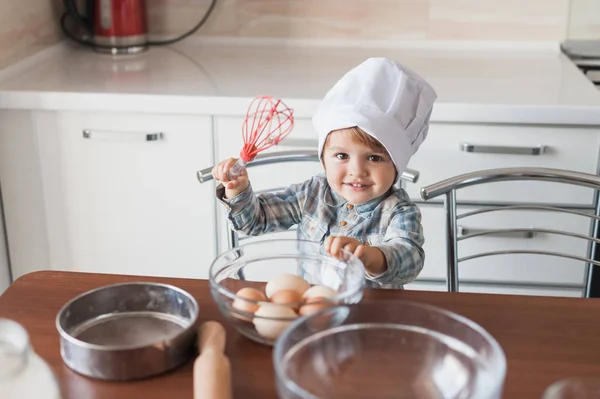 Adorable little kid in chef hat with whisk and eggs — Stock Photo