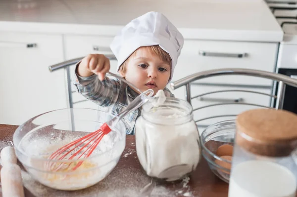 Criança pequena em chapéu de chef preparando massa na cozinha — Fotografia de Stock