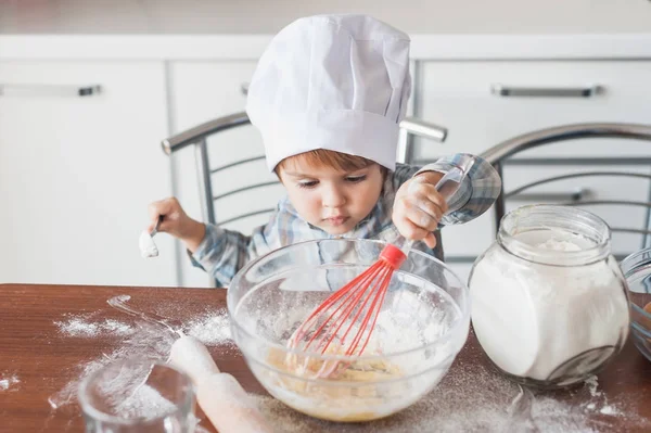 Little kid in chef hat mixturing dough with whisk at kitchen — Stock Photo