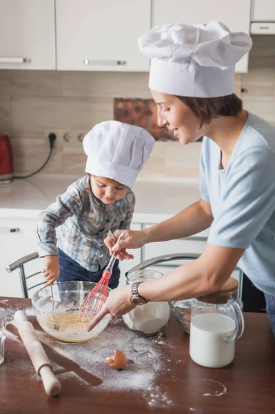 Glückliche junge Mutter und Kind mixen Teig mit Schneebesen in der Küche — Stockfoto