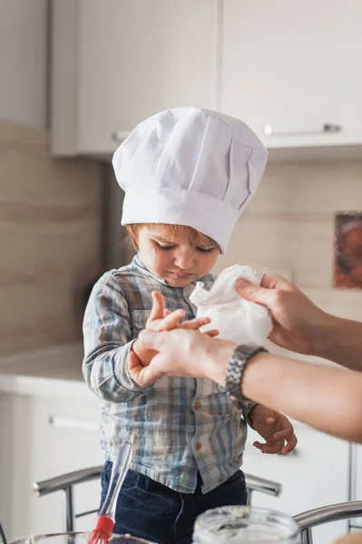 Madre limpiando las manos del niño en sombrero de chef después de cocinar - foto de stock