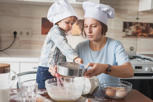 Junge Mutter und entzückendes Kind bereiten Teig auf chaotischem Tisch in der Küche zu — Stockfoto