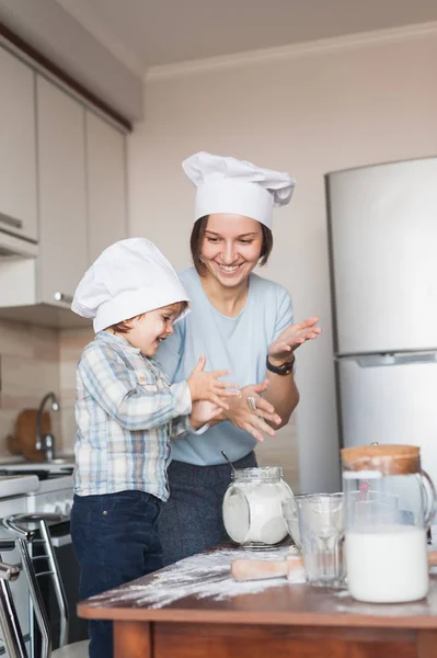 Madre e hijo aplaudiendo mientras preparan la masa en la cocina - foto de stock