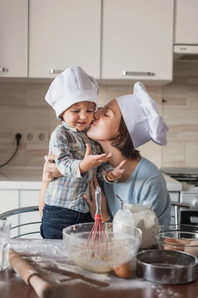 Мати цілує свою дитину, готуючи тісто на кухні — стокове фото