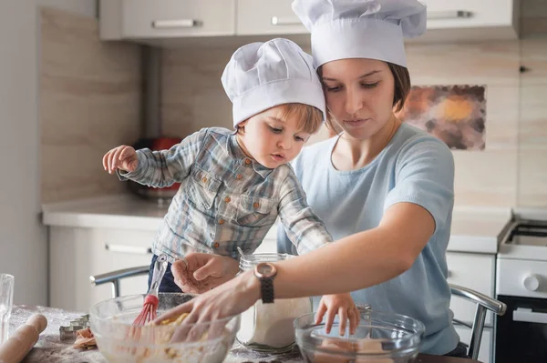 Mère et enfant dans des chapeaux de chef préparant la pâte à la cuisine — Photo de stock
