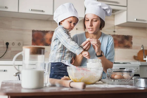 Mãe ensinando seu filho adorável como preparar massa na cozinha — Fotografia de Stock