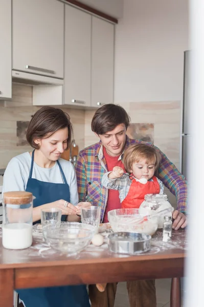 Família jovem feliz preparando massa na cozinha bagunçada — Fotografia de Stock