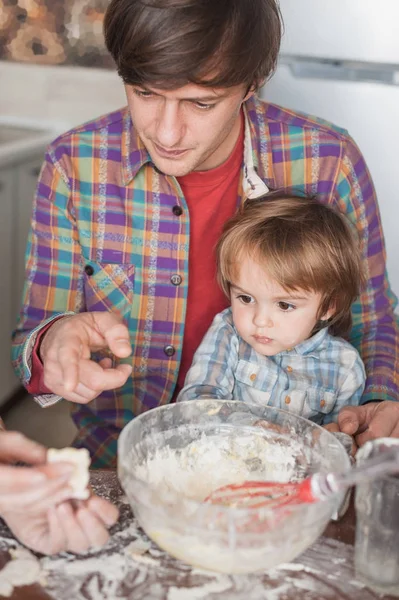 Padre e hijo mirando la galleta sin cocer en la mano de la madre - foto de stock