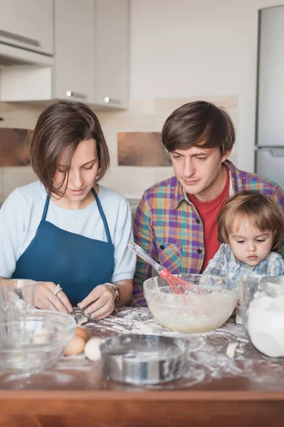 Hermosa familia joven preparando galletas en la cocina juntos - foto de stock