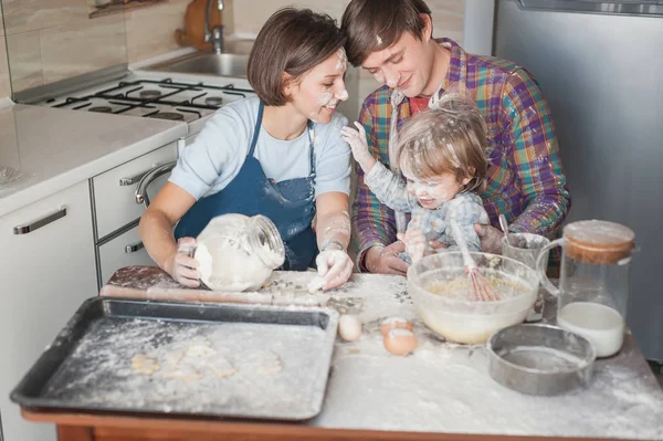 Familia joven divirtiéndose con harina en la cocina desordenada mientras hornea - foto de stock