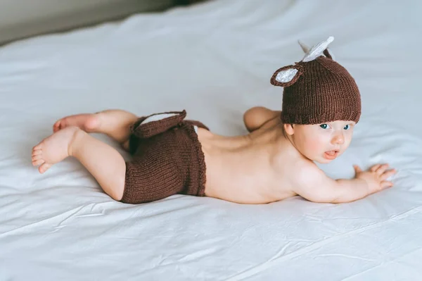 Infant child in knitted deer shorts and hat lying on tummy in bed — Stock Photo