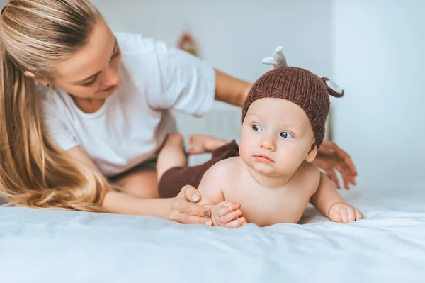 Мати сидить у ліжку зі своєю дитиною в трикотажному костюмі оленя — Stock Photo