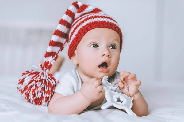 Adorabile bambino in cappello rosso e bianco a strisce con cervo giocattolo a letto — Foto stock