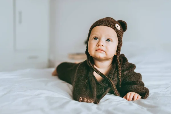 Beau bébé en bonnet en maille marron et couverture au lit — Photo de stock