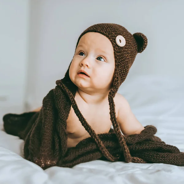 Criança infantil em chapéu de malha marrom com cobertor na cama — Fotografia de Stock